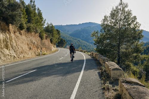 A professional cyclist riding a gravel bike on the empty road overlooking on mountains in Spain.
