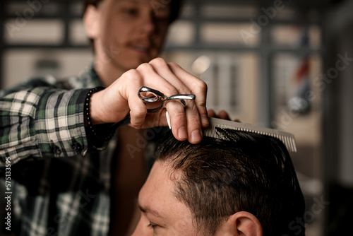 selective focus on hand of barber with hair scissors and comb neatly combing the wet hair of client