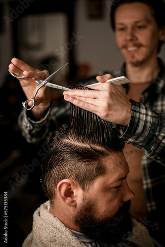 focus on hands of barber holding strand of hair and scissors and do haircut