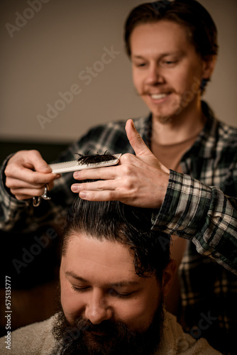Selective focus on hands of professional barber cutting and styling hair with comb to his client