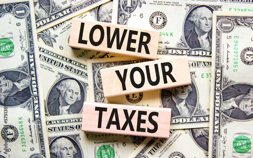 Lower your taxes symbol. Concept words Lower your taxes on wooden blocks on a beautiful background from dollar bills. Business tax lower your taxes concept. Copy space.