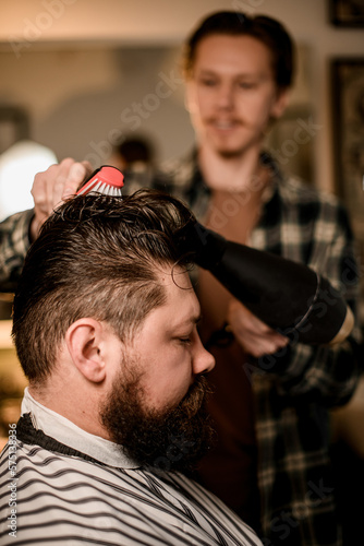 Close-up side view of the head being dries and styled by hairdresser with hair dryer and comb. Barbershop concept.