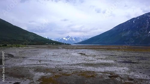 Aerial lifting up shot over shallow water and fjord towards mountain landscape in Norway