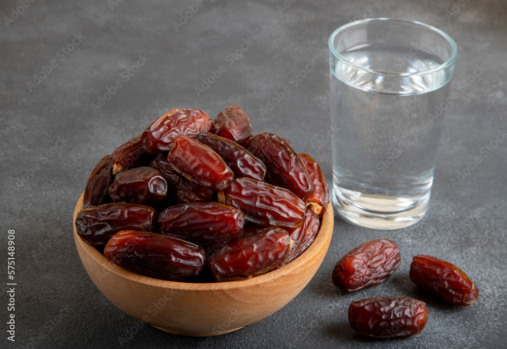 Glass of water with a bowl of date fruit on black background Glass of water with a bowl of date fruit on black background