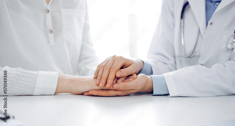 Doctor and patient sitting near each other at the table in clinic office. The focus is on female physician's hands reassuring woman, only hands, close up. Medicine concept Doctor and patient sitting near each other at the table in clinic office. The focus is on female physician's hands reassuring woman, only hands, close up. Medicine concept
