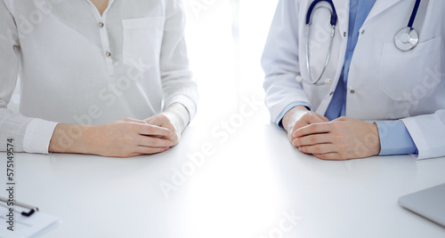 Doctor and patient sitting near of each other at the table in clinic, closeup. Medicine concept