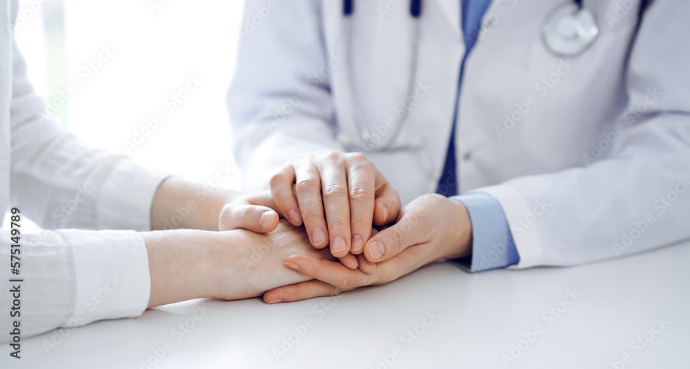 Doctor and patient sitting near each other at the table in clinic office. The focus is on female physician's hands reassuring woman, only hands, close up. Medicine concept Doctor and patient sitting near each other at the table in clinic office. The focus is on female physician's hands reassuring woman, only hands, close up. Medicine concept