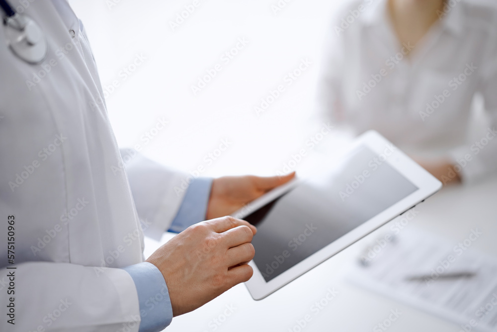 Doctor and patient in clinic. The focus is on female physician's hands using tablet computer at the background of unknown woman. Medicine concept Doctor and patient in clinic. The focus is on female physician's hands using tablet computer at the background of unknown woman. Medicine concept