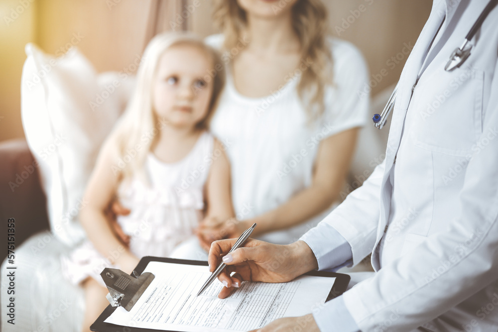 Doctor and patient. Pediatrician using clipboard while examining little girl with her mother at home. Happy cute caucasian child at medical exam. Medicine concept Doctor and patient. Pediatrician using clipboard while examining little girl with her mother at home. Happy cute caucasian child at medical exam. Medicine concept