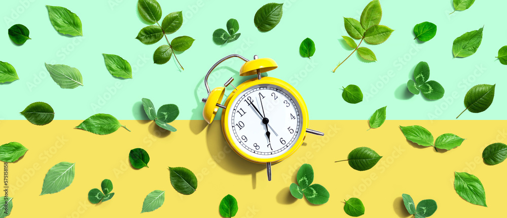 Yellow vintage alarm clock with green leaves - flat lay - obrazy, fototapety, plakaty 