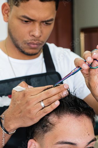 Hairdressing service performed by a man. Barber doing a haircut to a client. Young Latin American at work providing his services to clients. Colombian person working in his business