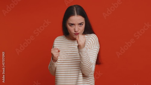 Angry aggressive pretty woman trying to fight at camera, shaking fist, boxing with expression, punishment, disappointment, rage, quarrel. Young adult girl isolated alone on red studio wall background