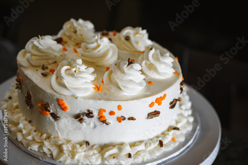 A homemade gourmet carrot cake with decorative white frosting  colored sprinkles and walnuts on a white cake stand