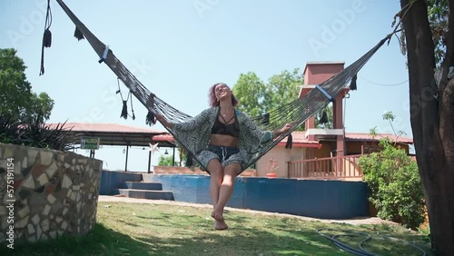 A young woman in a dress swings in a hammock, looking into the camera