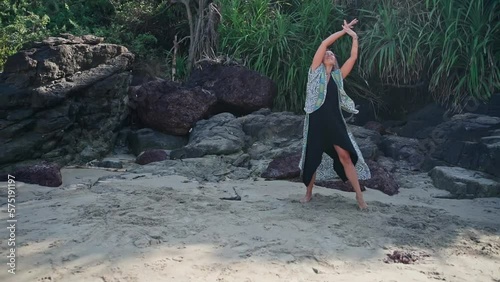 In this video, a woman in a pink outfit dances against the backdrop of hills.