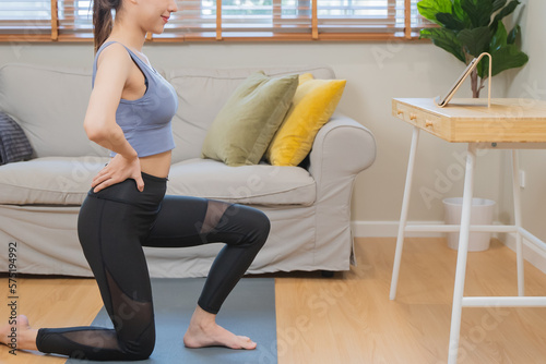 young woman watching exercise trainer in video online from touchpad and exercise at home