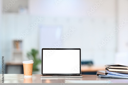 Bright office interior with laptop computer on wooden desk. Blank screen for graphic display montage