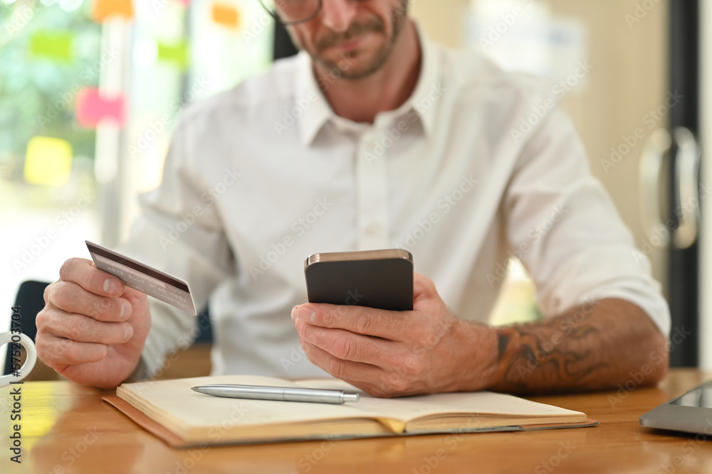 Cropped shot of man hand holding credit card shopping online, making payment for purchase on mobile phone