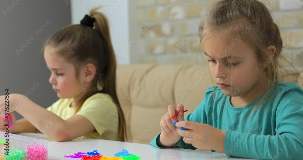 Two girls weaving bracelets made of multicolored rubber bands Two girls weaving bracelets made of multicolored rubber bands