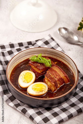 Egg and Pork in Sweet Brown Sauce in bowl  placed on tablecloth, 2 boiled eggs, braised pork and cilantro. popular food in asia.