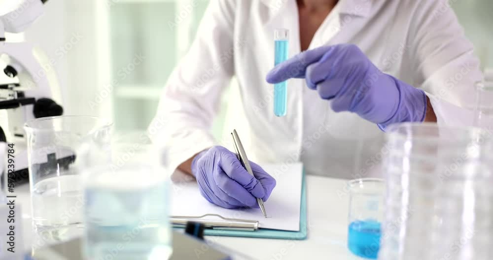 Doctor holds test tube with blue liquid and writes chemical report Doctor holds test tube with blue liquid and writes chemical report