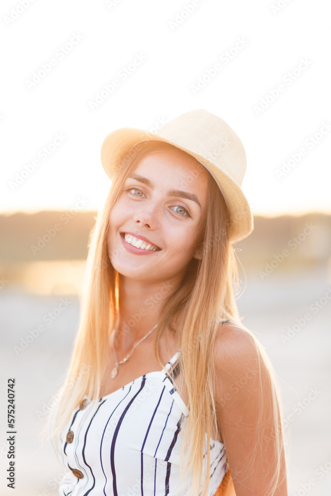 young blonde in a hat and summer dress on the beach