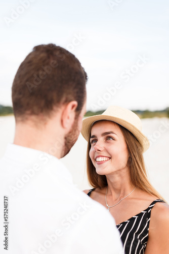 young blonde woman in a hat looks at her partner on a sunny beach