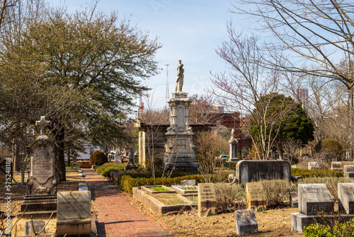 A gorgeous winter landscape in the graveyard with headstones, graves, bare winter trees, lush green trees, plants and flowers at the Oakland Cemetery with a blue sky and clouds in Atlanta Georgia USA photo