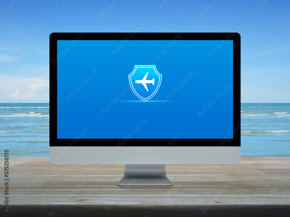 Airplane with shield flat icon on desktop modern computer monitor screen on wooden table over tropical sea and blue sky with white clouds, Business travel insurance and safety online concept Airplane with shield flat icon on desktop modern computer monitor screen on wooden table over tropical sea and blue sky with white clouds, Business travel insurance and safety online concept