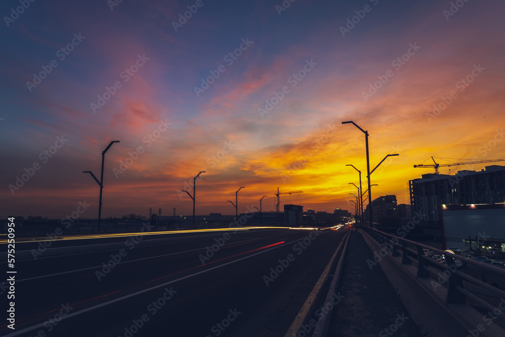 City road with a view of the sky with a sunset and traces of lanterns from cars