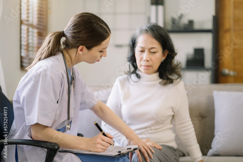 Female doctor in white medical coat discussing elderly patient in clinic, therapist. Consulting woman examining knee pain, health care, medicine concept.