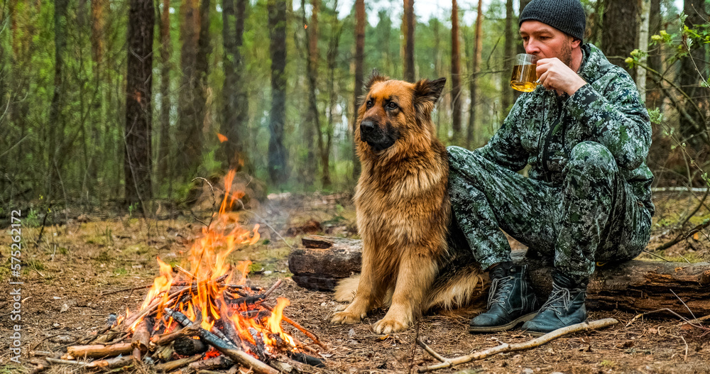 Foto Stock Adult Man is relaxing at the fire with his dog in the nature ...