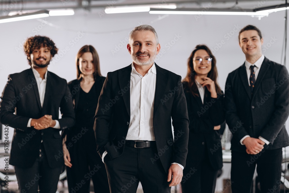 Confident company ceo standing in front of employees. Smiling coworkers posing with their boss in office. International business team Confident company ceo standing in front of employees. Smiling coworkers posing with their boss in office. International business team