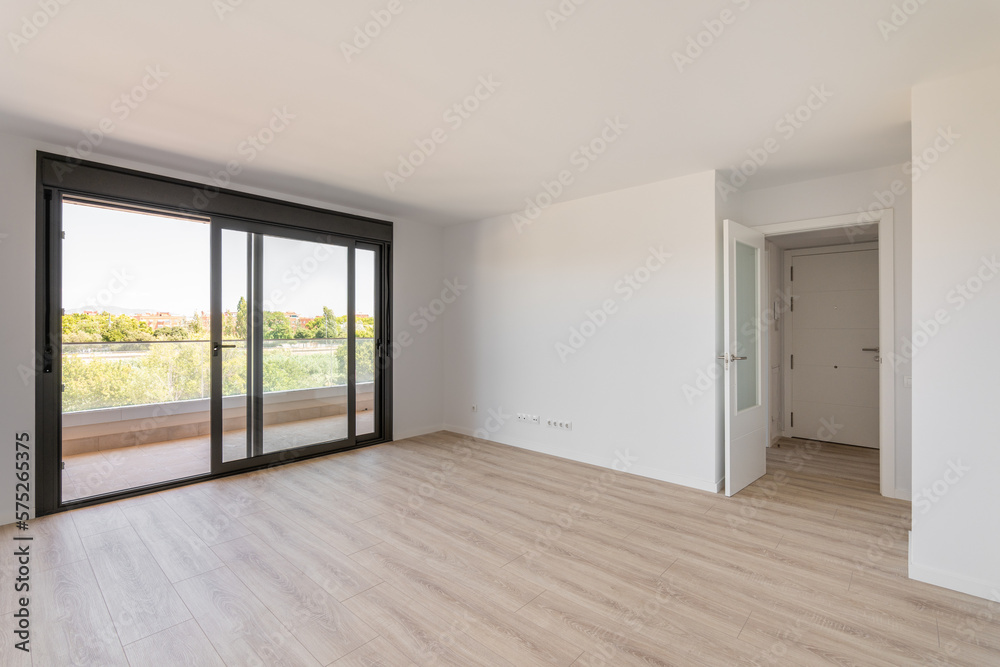 Spacious large room with wooden parquet structure and panoramic window overlooking beautiful landscape among complex of new buildings and balcony with elegant glass border. Mortgage and moving concept Spacious large room with wooden parquet structure and panoramic window overlooking beautiful landscape among complex of new buildings and balcony with elegant glass border. Mortgage and moving concept
