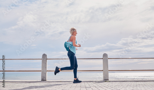 Fototapeta Naklejka Na Ścianę i Meble -  Senior woman running outdoor at beach promenade, sky mockup and energy for health, wellness and workout. Elderly female, exercise and runner at ocean for sports training, fitness and cardio marathon