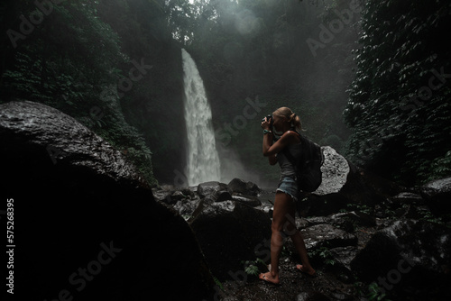 Young woman tourist taking photo of the Nung Nung waterfall, magic island of Bali, Indonesia.