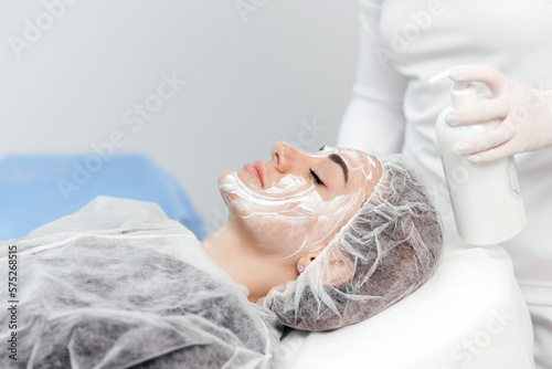 Photos Cosmetologist is applying cream with anesthesia on patient's face skin before biorevitalization procedure