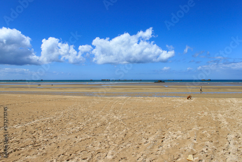 Beach and seascape with blue sky and sun. A landing beach in Normandy with the pontoon bridge from the Second World War in the distance.