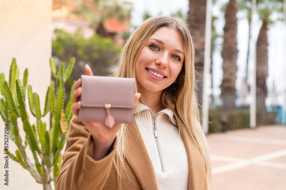 Fototapeta premium Young pretty blonde woman holding a wallet at outdoors with happy expression