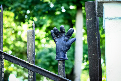 One black leather glove with splayed fingers put on a tip of a fence in a park