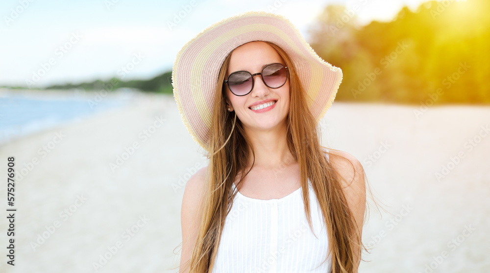 Portrait of a happy smiling woman in free happiness bliss on ocean beach standing with a hat and sunglasses. A female model in a white summer dress enjoying nature