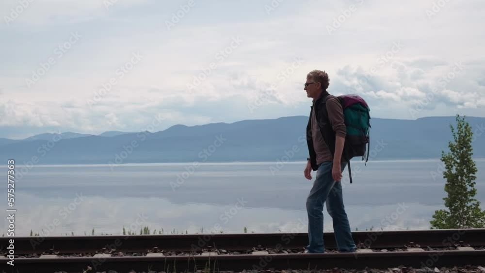 middle aged man with backpack walks along the rails of an old railway along Lake Baikal. slow motion. local travel, exploring new places and hiking on weekends. active recreation, concept of tourism. middle aged man with backpack walks along the rails of an old railway along Lake Baikal. slow motion. local travel, exploring new places and hiking on weekends. active recreation, concept of tourism.