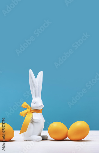 Sticker White Easter bunny with yellow ribbon bow with dyed orange eggs on white table