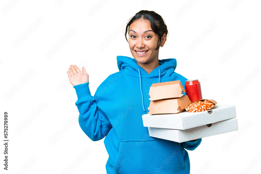 Young Uruguayan woman holding pizzas and burgers over isolated chroma key background extending hands to the side for inviting to come Young Uruguayan woman holding pizzas and burgers over isolated chroma key background extending hands to the side for inviting to come