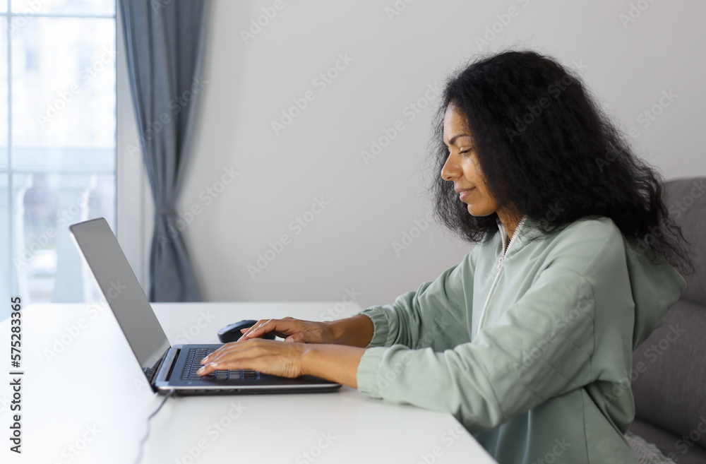 Freelance programmer coding on a laptop at home. Focused black woman typing text on modern computer with a smile Freelance programmer coding on a laptop at home. Focused black woman typing text on modern computer with a smile