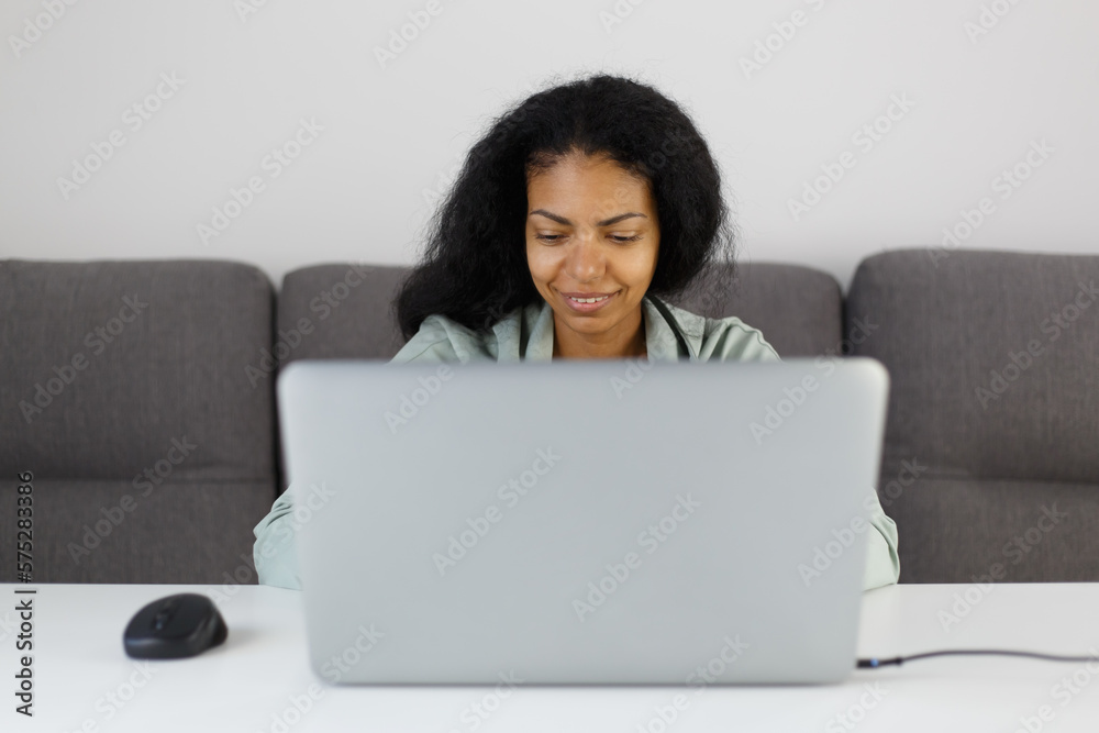 Young adult POC female works on silver laptop. Cheerful black woman working on modern notebook computer at home Young adult POC female works on silver laptop. Cheerful black woman working on modern notebook computer at home