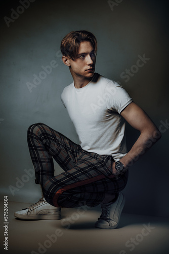 male fashion model crouch and pose deliberate in studio, showcasing his chiseled features and impeccable style while his confident gaze exudes a sense of cool sophistication and look to right side