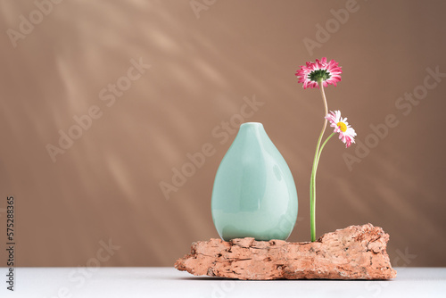 Two daisy spring flowers near a tiny green vase on a rock on table. Misplaced eccentric. Fragile. assumptions. Unordinary. Brown background with copy space. Blooming flowers. Greeting card. sunlight photo