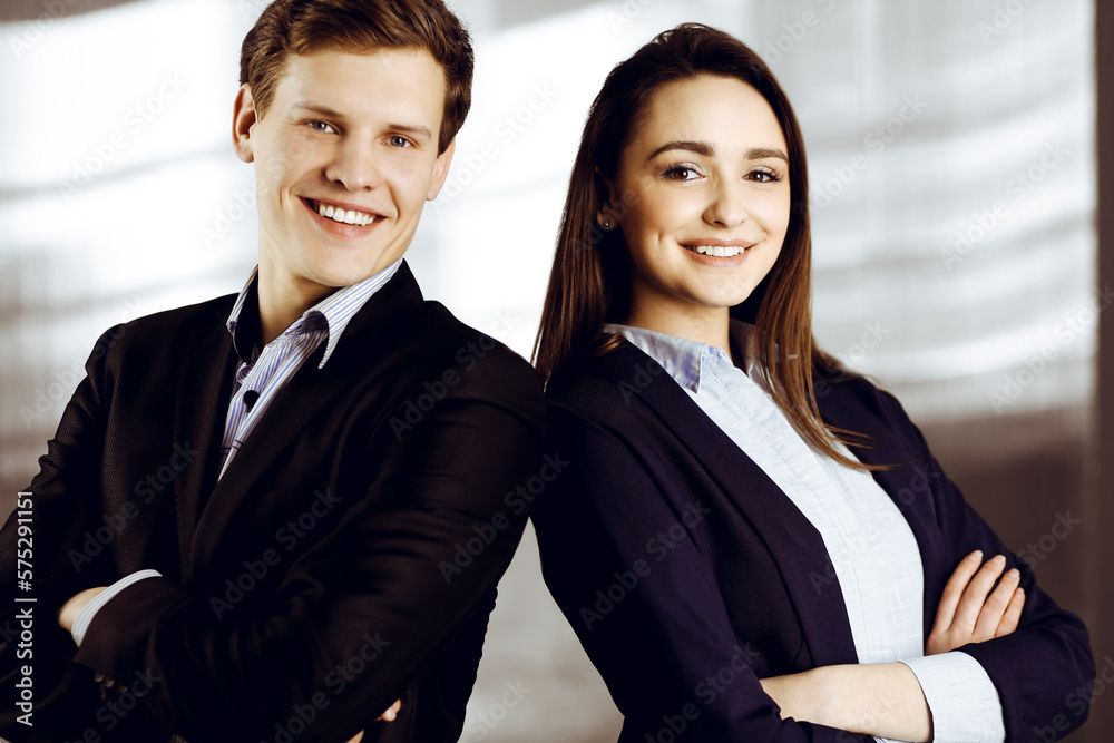 Friendly young colleagues are standing as a team with crossed arms in a modern office. Portrait of successful business people at work Friendly young colleagues are standing as a team with crossed arms in a modern office. Portrait of successful business people at work