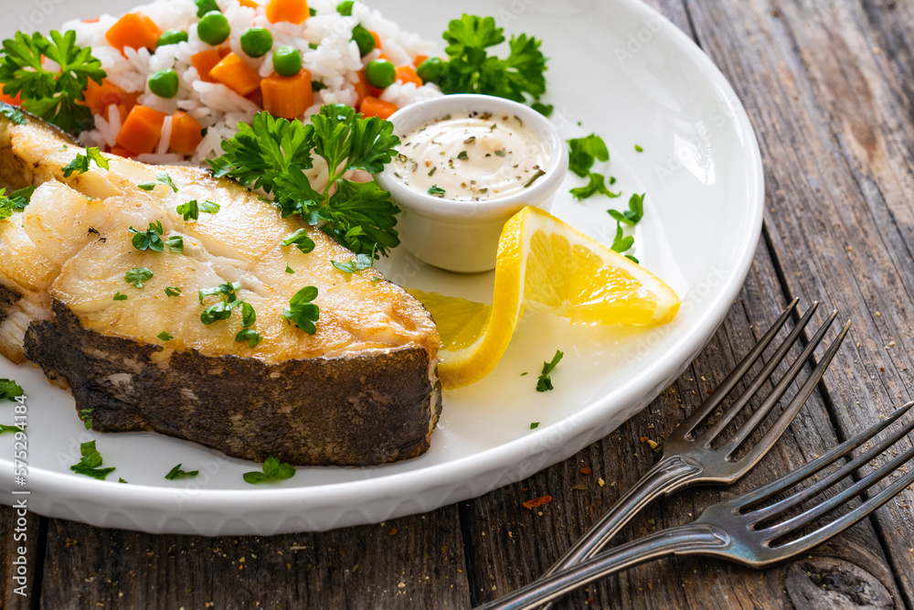 Fish dish - fried halibut with white rice, peas and carrots on wooden table
